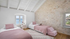 Une chambre avec deux lits, un mur en pierre, une fenêtre et un plafond blanc.