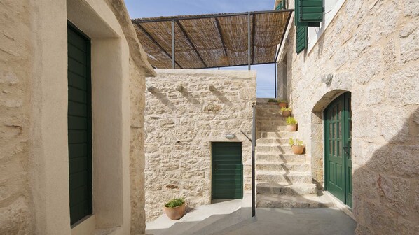 A narrow alleyway with stone buildings, green shutters, and potted plants.