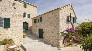 A stone building with a staircase leading to a door, a chair, and a potted plant. - Villa Lapis by MyWaycation (Zavala)