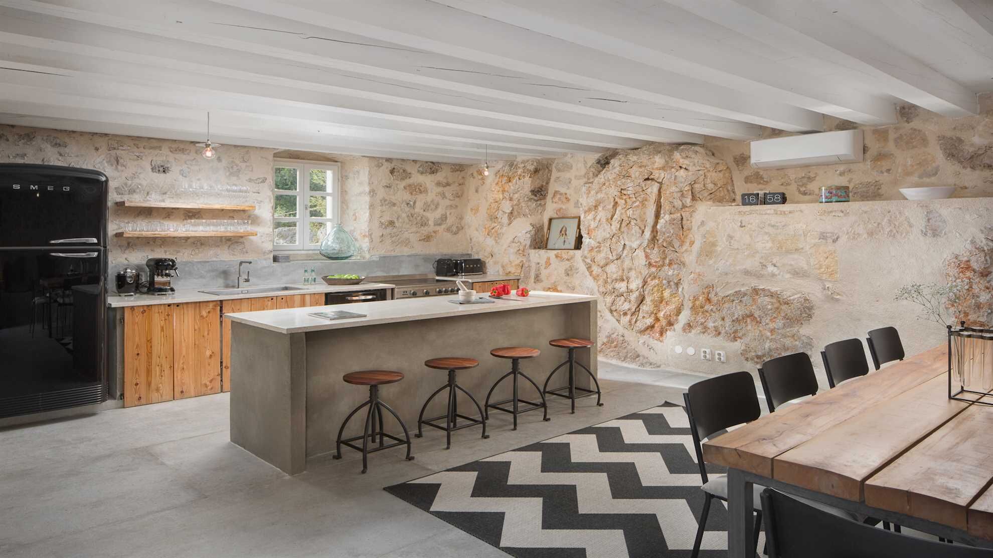 A modern kitchen with a central island, bar stools, a dining table, and a stone wall.