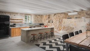 A modern kitchen with a central island, bar stools, a dining table, and a stone wall.