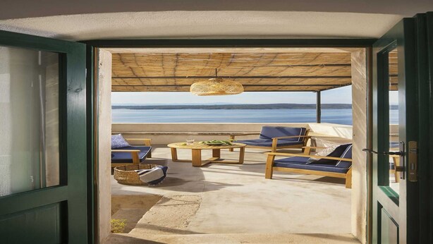 An open doorway leading to a covered outdoor seating area with a view of the sea.