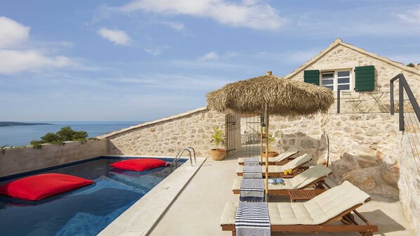 Une villa en pierre dotée d’une piscine, de chaises longues et offrant une vue sur la mer.