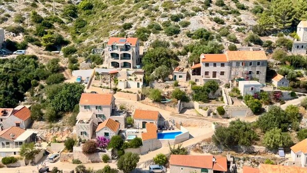 Un pueblo costero con edificios de piedra, una piscina central y casas escalonadas.