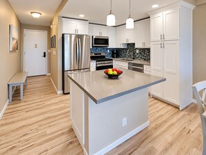 A modern kitchen with a central island, stainless steel appliances, and a tiled backsplash. - Airy Kihei Renovated Condo Ocean Views Spacious Lanai Near Kamaole Beach (Kihei)