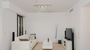 A modern living room with a white sofa, a coffee table, a flat-screen TV, and a ceiling light fixture. - ✽ Jerusalem Suites Mamilla ✽ (Jerusalem)