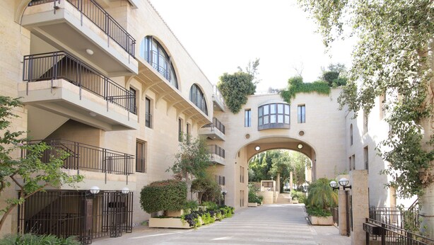 A building with multiple balconies, an arched entrance, and surrounding greenery. - ✽ Jerusalem Suites Mamilla ✽ (Jerusalem)