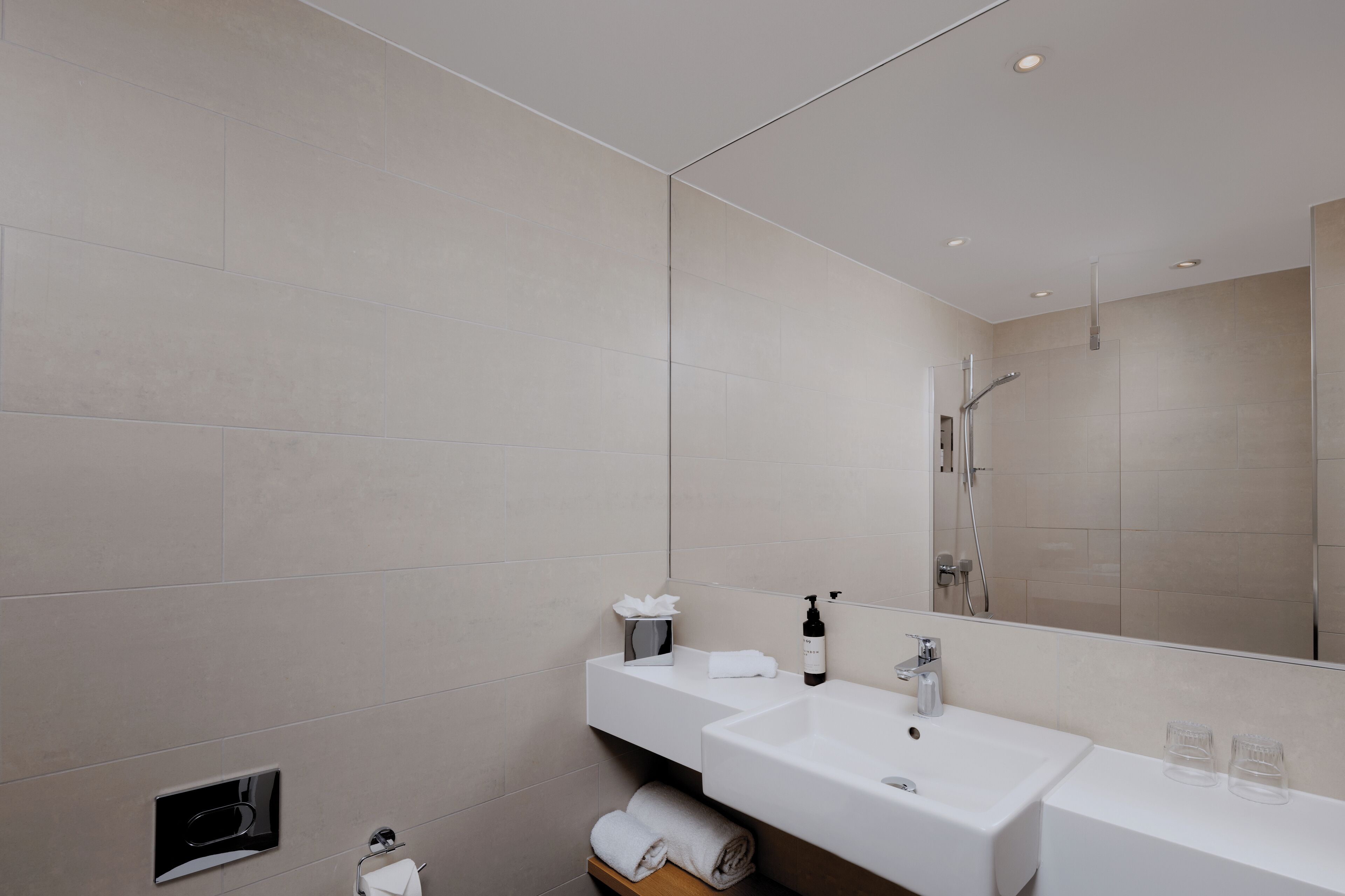 A modern bathroom with a large mirror, two sinks, and a shower.