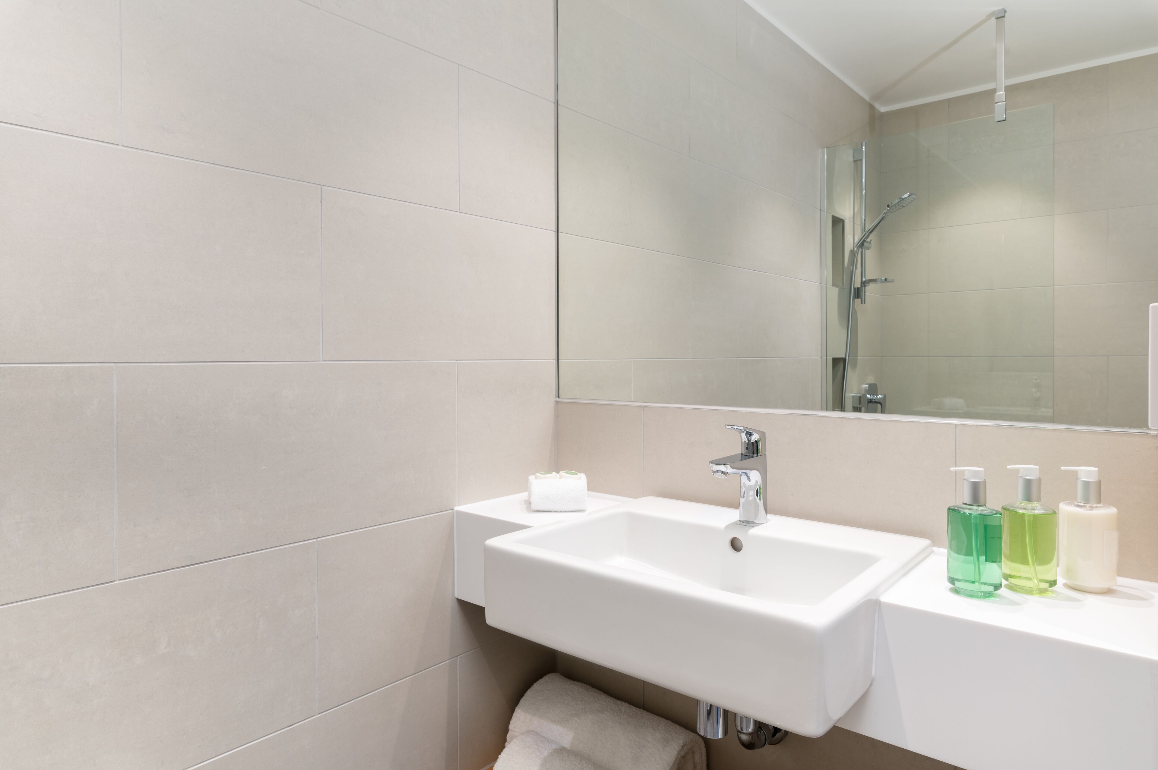 A modern bathroom with a white sink, a mirror, and three bottles of liquid soap.
