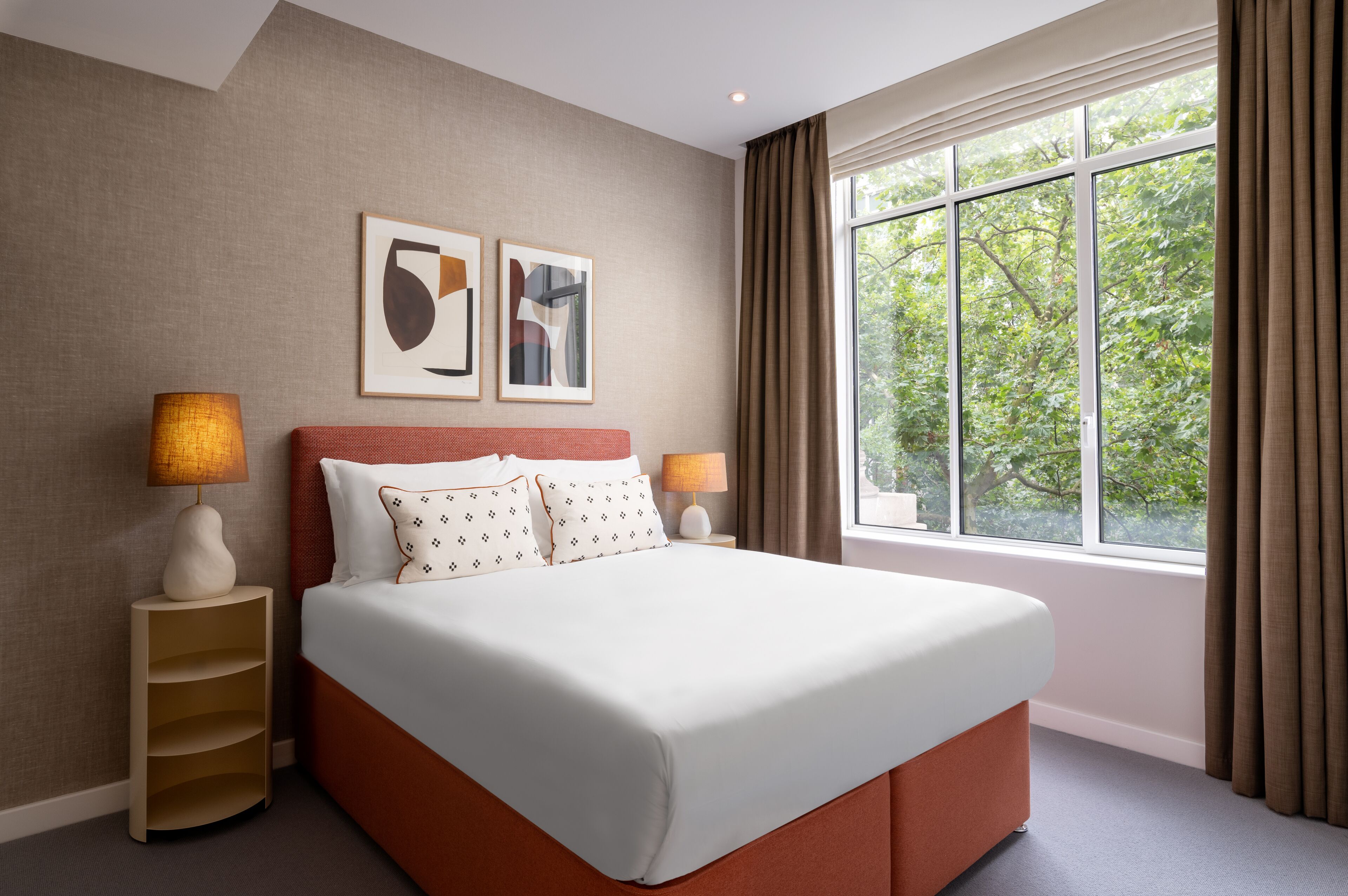 A neatly arranged hotel room with a large bed, two bedside lamps, a nightstand, and a window with curtains.