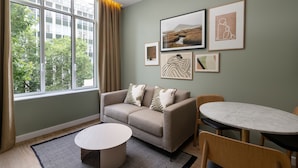 A modern living room with a sofa, a round table, and a window with curtains. - The Lincoln Suites (London)