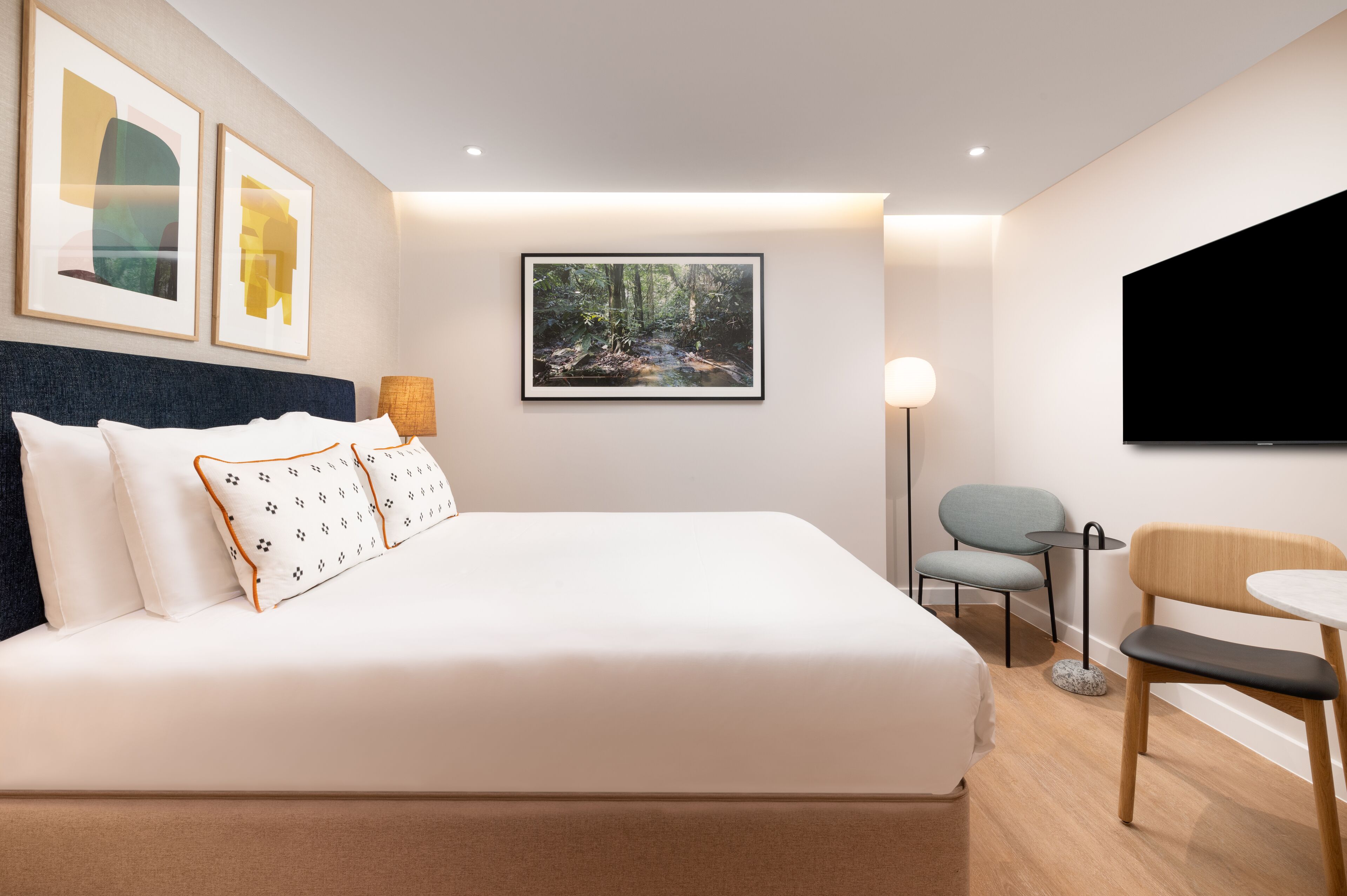 Ein modernes Hotelzimmer mit einem großen Bett, einem Schreibtisch, einem Sessel und einem Fernseher.