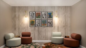 Un intérieur moderne avec un mur lambrissé en bois, six œuvres d’art encadrées et trois espaces de détente circulaires, chacun comprenant une petite table et deux lampes fixées au mur.