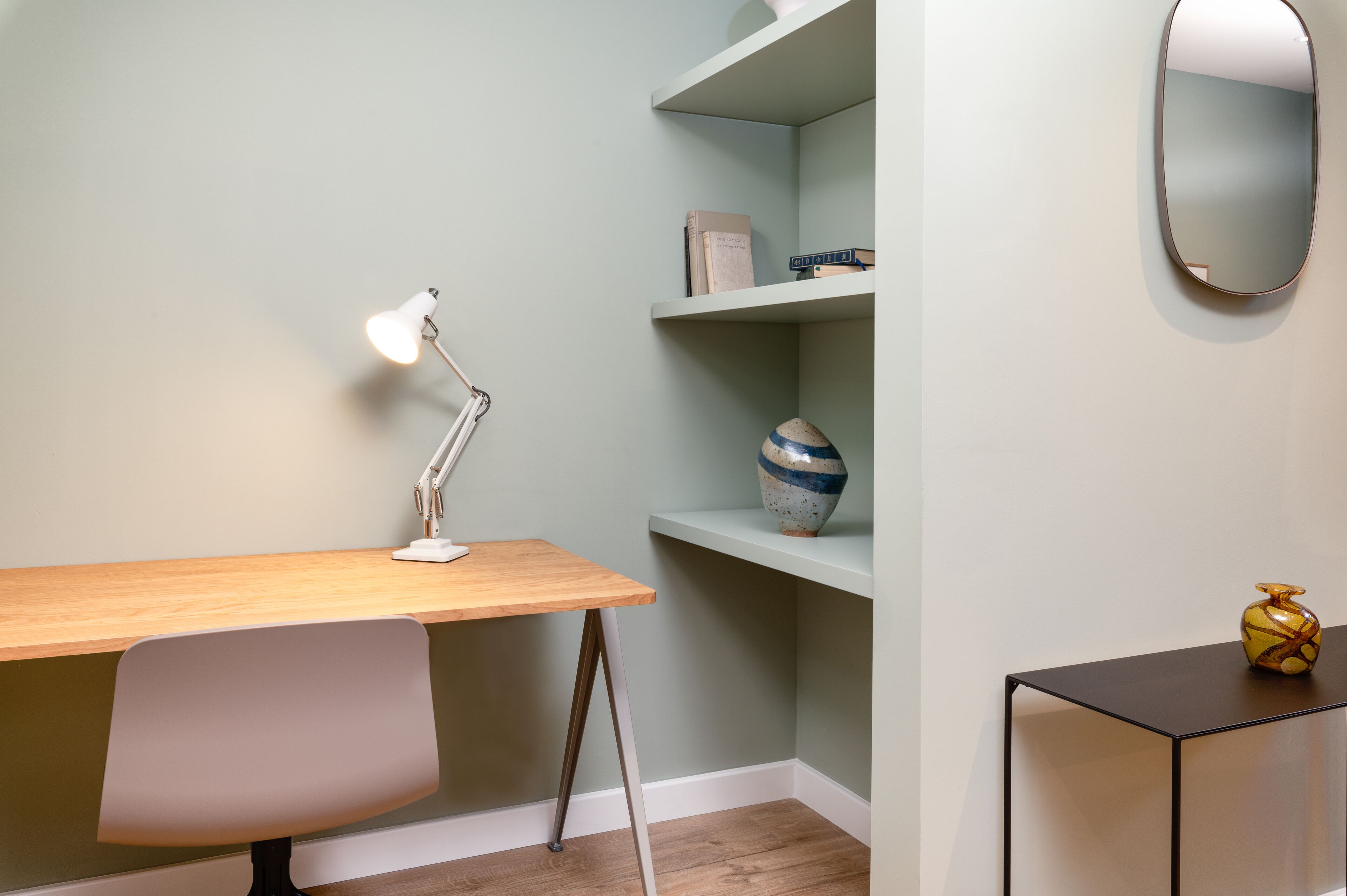 Un espacio de trabajo con escritorio, silla, estanterías y espejo.