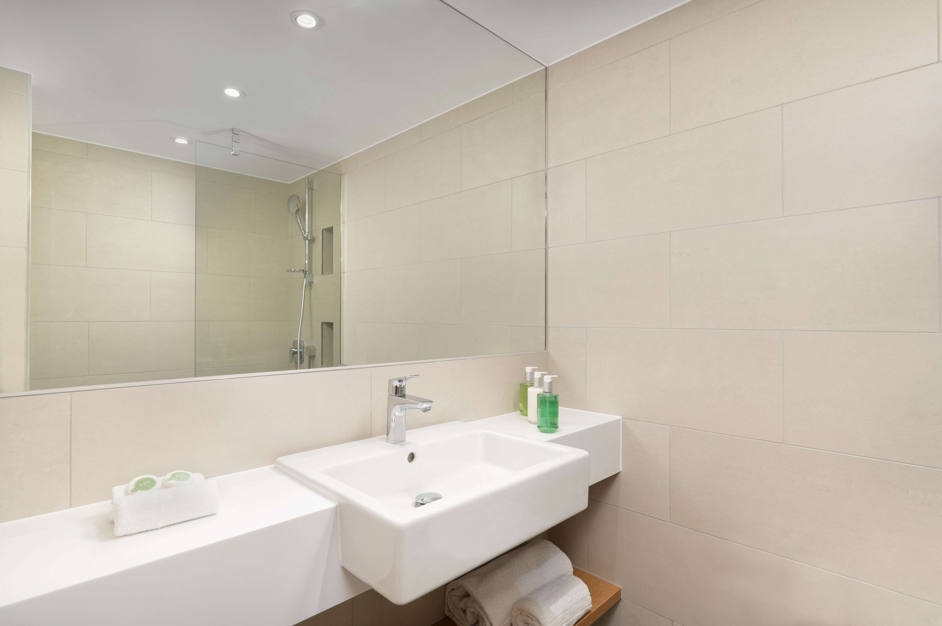 A modern bathroom with two sinks, a large mirror, and a shower.