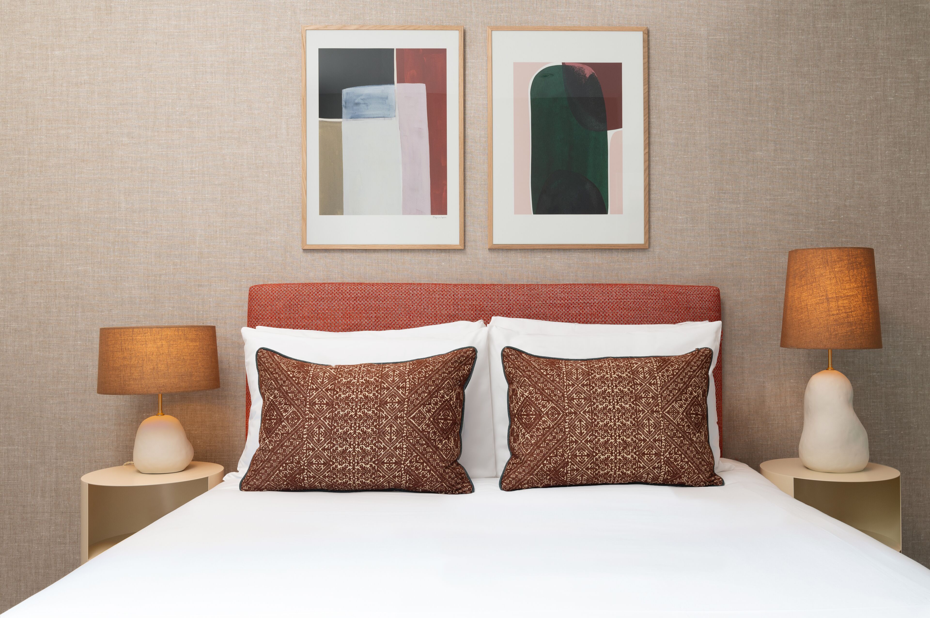 A neatly arranged hotel room with a large bed, two side tables with lamps, and two framed abstract artworks on the wall.
