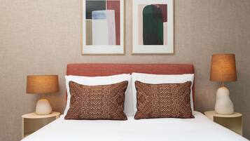 A neatly arranged hotel room with a large bed, two side tables with lamps, and two framed abstract artworks on the wall.