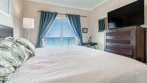 A hotel room with a large bed, a television, a dresser, and a window with curtains.