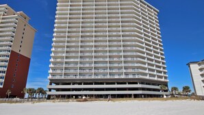 A multi-story hotel with balconies on each floor, located near a beach.
