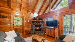 Ein gemütliches Blockhaus-Interieur mit Kamin aus Stein, Holzwänden, einem Fernseher und einer Couch.