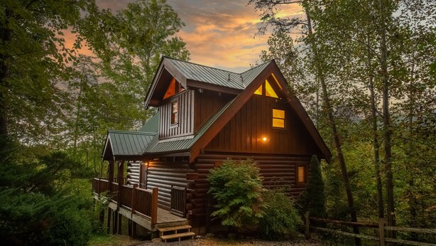 Eine rustikale Holzhütte mit Veranda und Schornstein, umgeben von dichtem Wald.