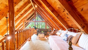 Ein gemütliches Schlafzimmer unter dem Dach mit Holzbalkendecke, einem großen Fenster, einer Couch und einem Bett.