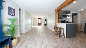 Una cocina amplia con electrodomésticos modernos y una isla central, un pasillo con suelo de madera y una planta en maceta.