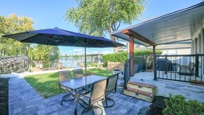 Un patio con mesa y sillas, un espacio cubierto y vista a un lago.