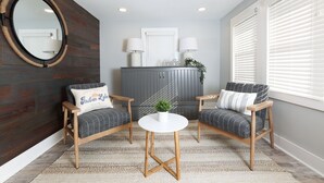 Una habitación con dos sillones, una mesa redonda, un espejo y un aparador con dos lámparas.