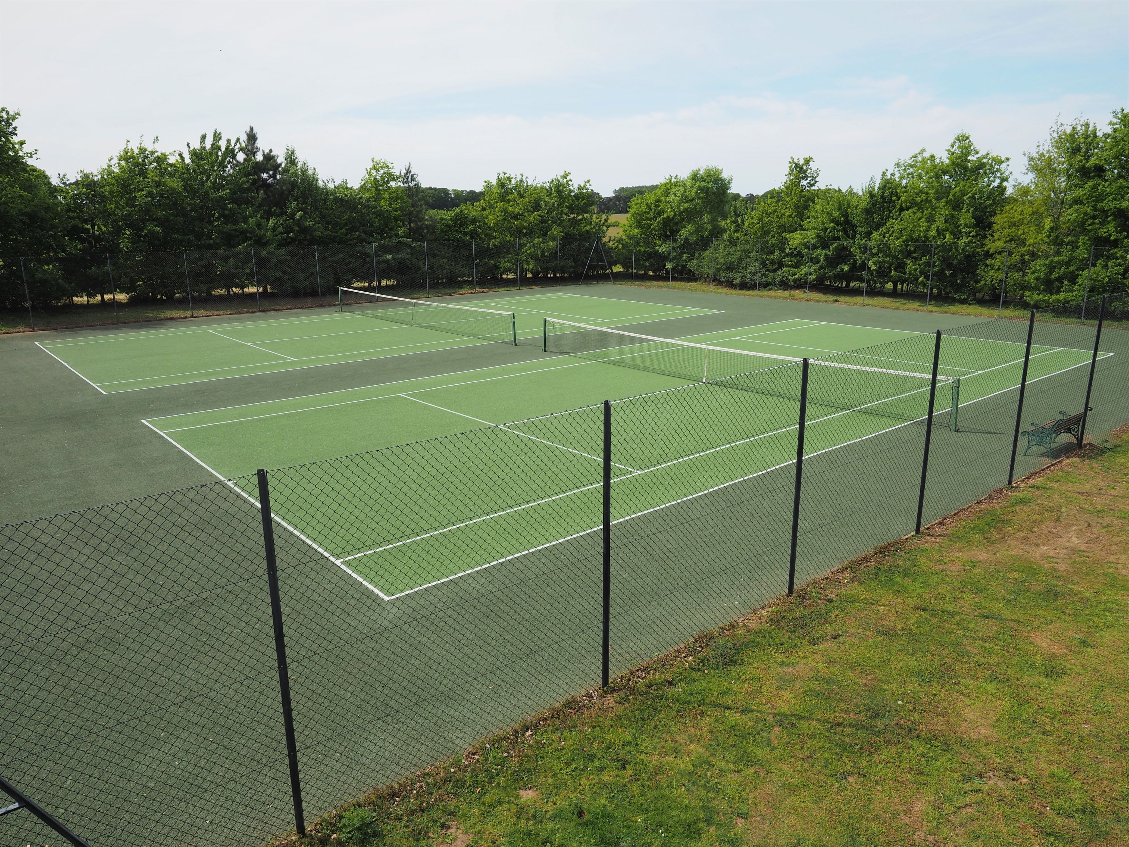 A tennis court with a net, surrounded by a fence and trees.
