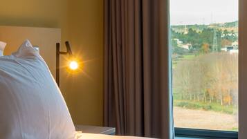 Una habitación de hotel con cama, mesita de noche, lámpara y ventana con cortinas.