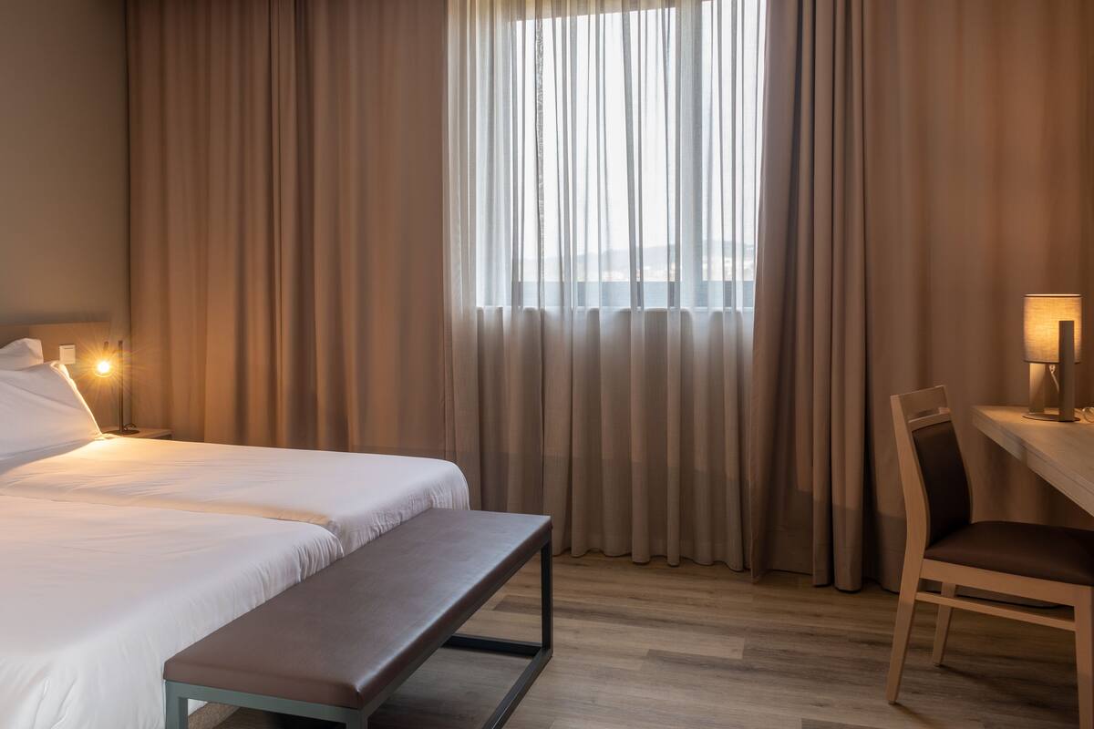 A hotel room with a bed, a bench, a desk, and a chair.