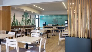 L’intérieur d’un restaurant moderne est agrémenté de tables et de chaises en bois, d’un mur bleu orné d’une fresque représentant un arbre, et d’un espace comptoir avec une machine à café.