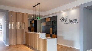 Un hall d'accueil moderne avec un comptoir d'accueil en bois, une enseigne murale indiquant « MEU HOTEL PORTOGANDRA » et une cloison en lattes de bois.