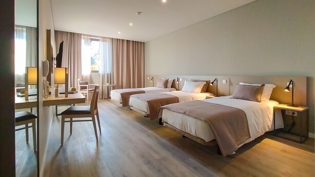 Une chambre d’hôtel avec deux lits, un bureau avec une chaise, un téléphone et une fenêtre avec des rideaux.