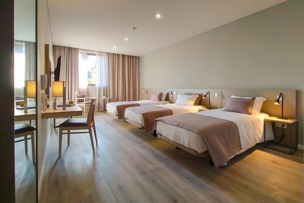 A hotel room with two beds, a desk with a chair, a telephone, and a window with curtains.