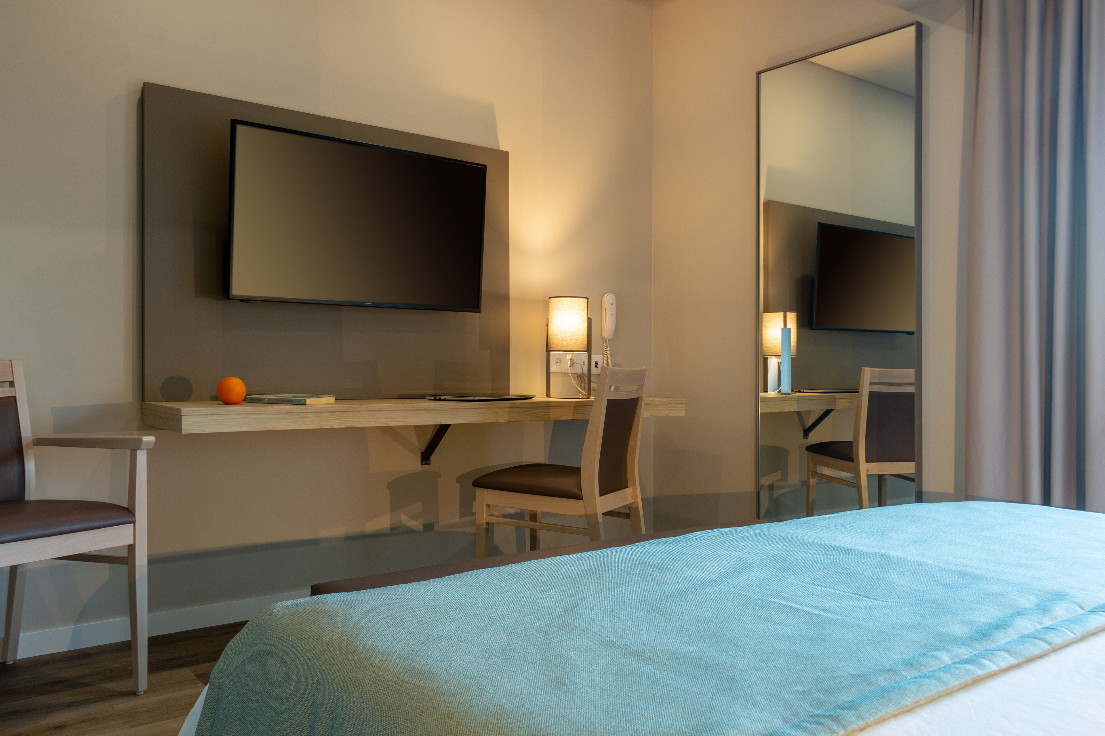 Une chambre d’hôtel comprenant un lit, un bureau avec une chaise, un téléviseur à écran plat fixé au mur et une table de chevet avec une lampe.