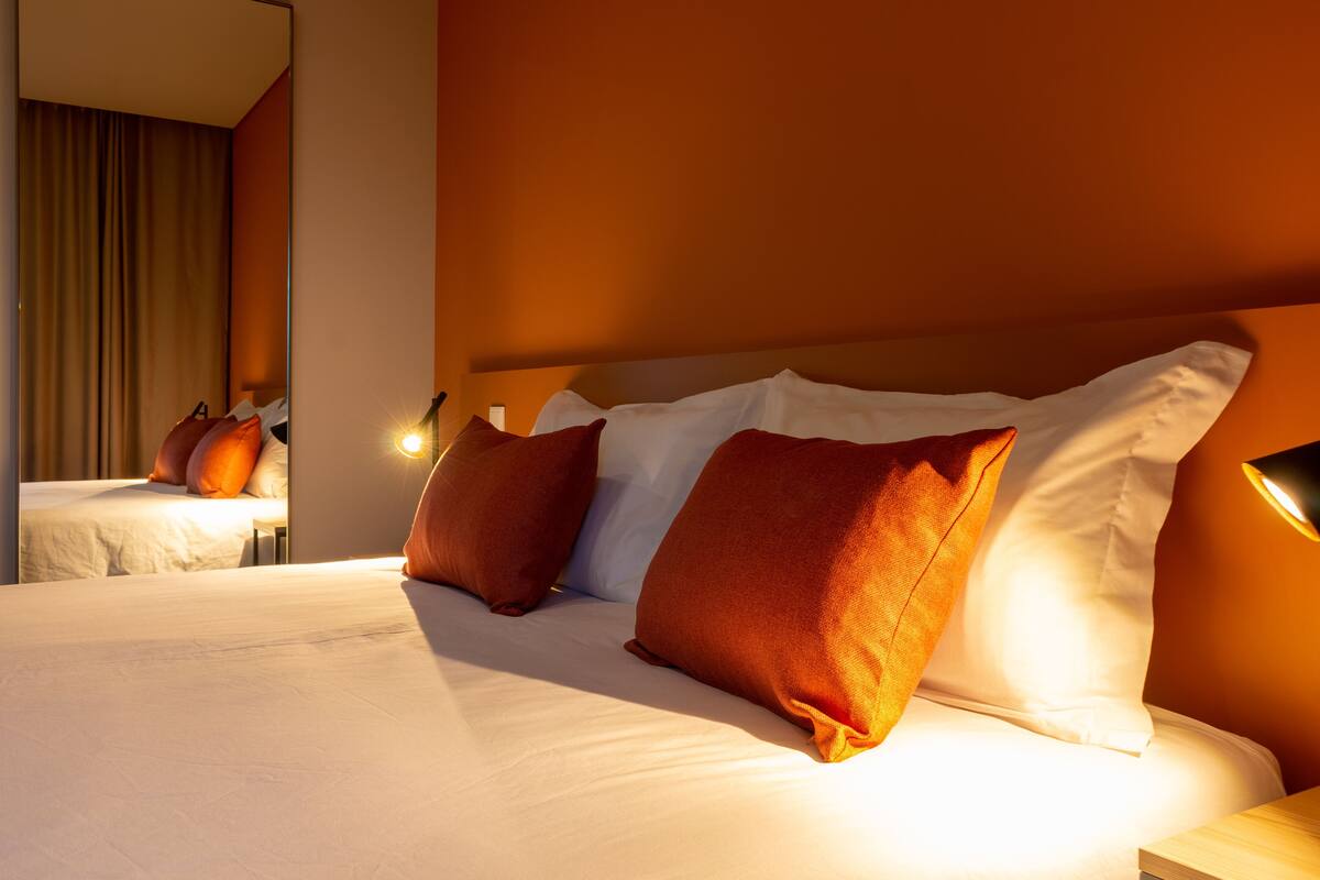 A hotel room with a large bed, multiple pillows, and a nightstand with a lamp.
