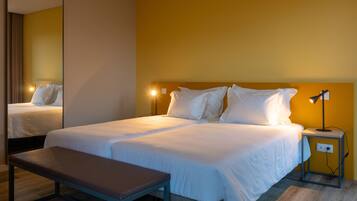 A hotel room with a large bed, a bedside table, a bench, and a nightstand with a lamp.