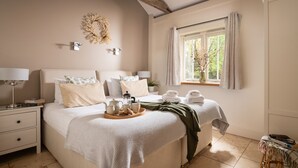 A neatly arranged bedroom with a bed, bedside tables, a window with curtains, and a wall-mounted light fixture. - 3 bedroom single story barn with luxury indoor pool close to North Norfolk coast (Fakenham)