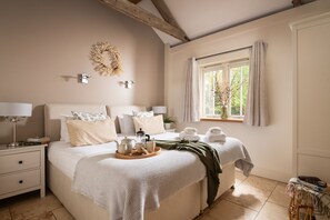 Um quarto bem arrumado com uma cama, mesas de cabeceira, uma janela com cortinas e um ponto de luz na parede.