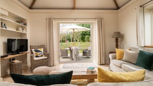 A living room with a television, sofa, and a view to an outdoor patio. - 3 bedroom single story barn with luxury indoor pool close to North Norfolk coast (Fakenham)