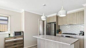 A modern kitchen with a central island, stainless steel appliances, and wooden cabinetry. - Relax at Torquay Dunes: Shops and Beaches Nearby (Torquay)