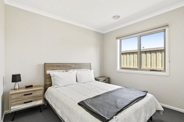Une chambre à coucher avec un lit, une table de chevet, une lampe et une fenêtre donnant sur une clôture.