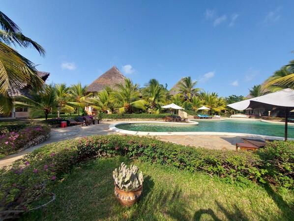 A resort with a swimming pool, palm trees, and a thatched-roof structure. - Tembo Court Apartment (Malindi)