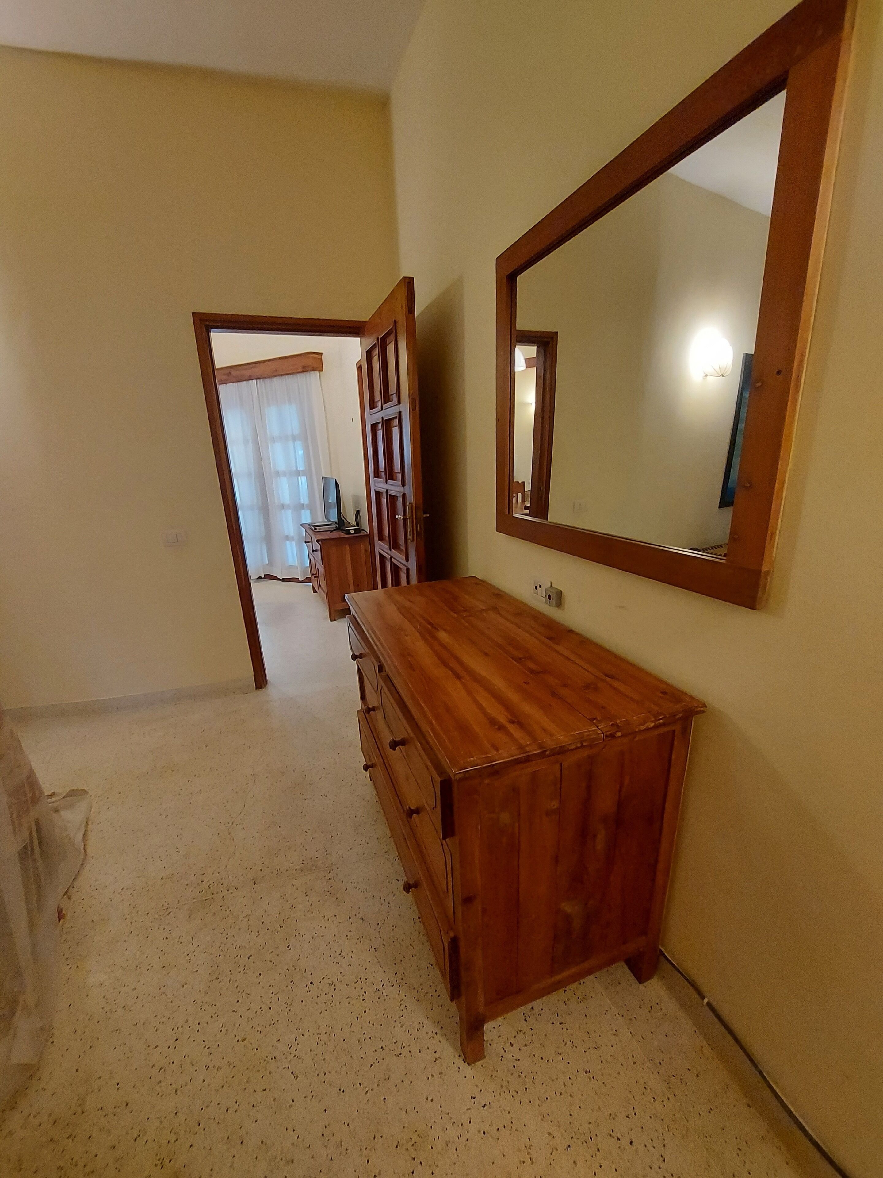 A room with a wooden dresser, a large mirror, and a door leading to another room.