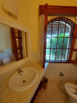 A bathroom with a large mirror, a sink, and a toilet. There is a window with a view of greenery outside. - Tembo Court Apartment (Malindi)