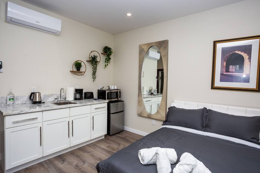 Een moderne hotelkamer met een bed, een grote spiegel, een kitchenette met een spoelbak en een koffieapparaat.
