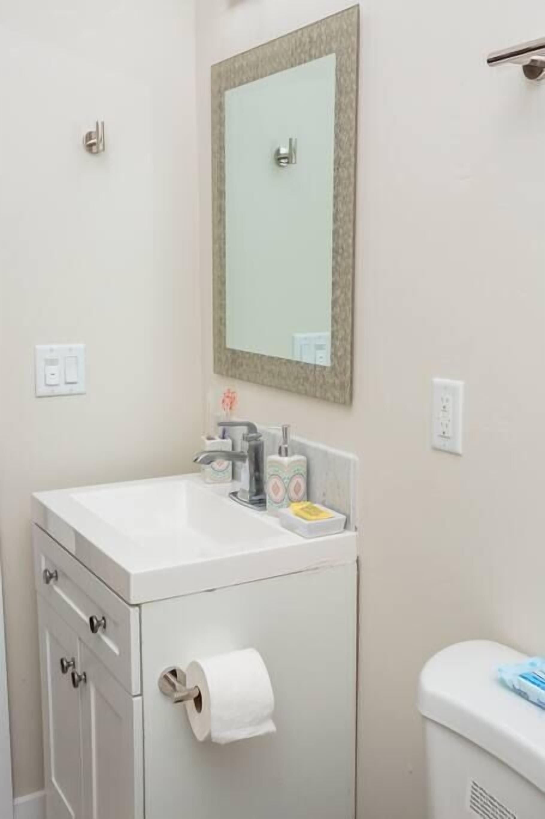 A bathroom with a white sink, a mirror, a toilet, and a cabinet with drawers.