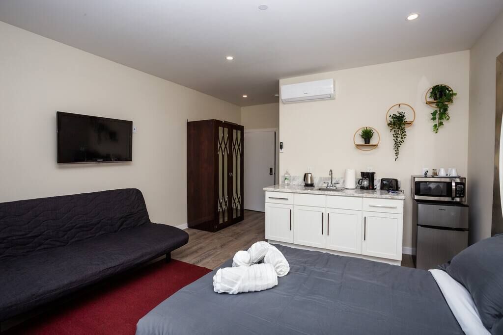 Een moderne hotelkamer met een bed, een bank, een kitchenette en een televisie.